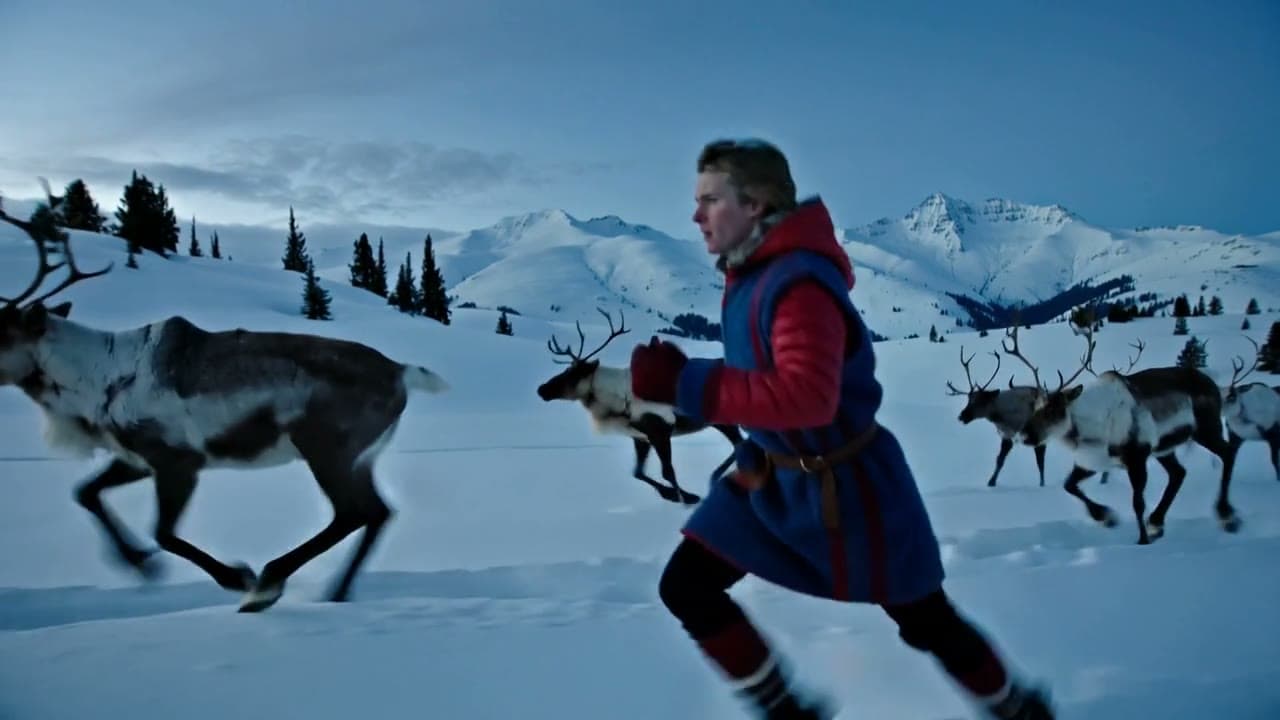 A herder runs beside reindeer across the snow at blue hour