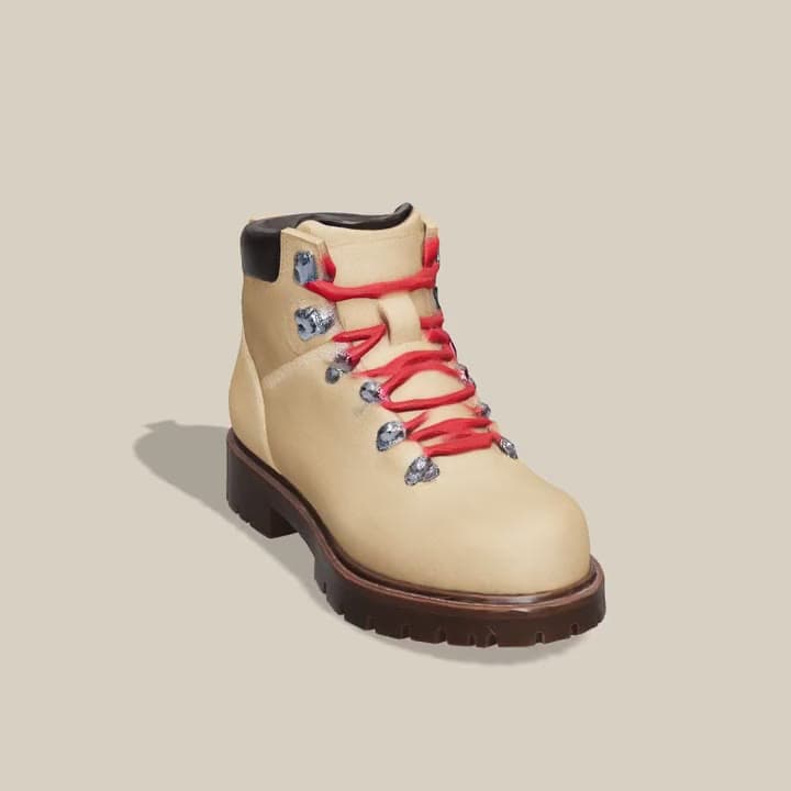 A 3D model of a tan suede hiking boot with red laces, turning on a stand