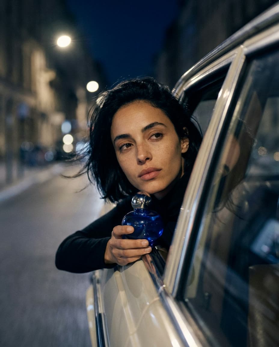 A woman with a sleek black bob leans out of a car window on a city street at night